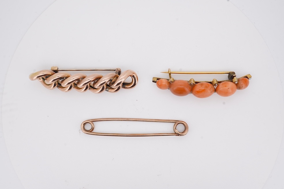 An early 20th century yellow metal and graduated five stone coral bead brooch, with seed pearl spacers, 45mm, together with a yellow metal curb link brooch and a yellow metal (stamped 9c) safety pin. Condition - fair